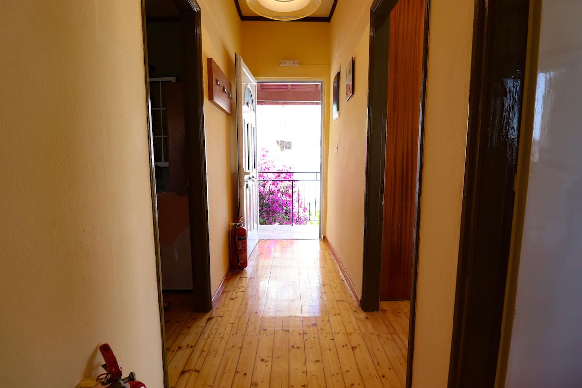 Un couloir doté d’un plancher en bois et d’une porte donnant sur un espace extérieur agrémenté de fleurs roses.