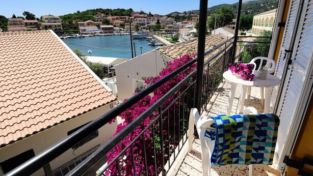 A balcony with a tiled roof, a white chair with a patterned towel, and a table with pink flowers. - Antigoni Apartments (Corfu)