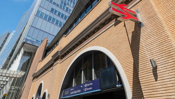 A building with a prominent glass facade and a brick structure with a sign for the London Bridge Station. - Tower Bridge Modern 2Bed 2Bath Apartment by London Bridge (London)