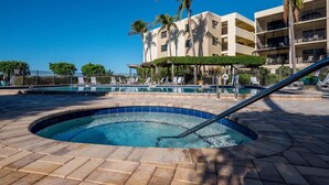 Ein Hotelpoolbereich mit Whirlpool, Liegestühlen, Palmen und einem mehrstöckigen Gebäude im Hintergrund.