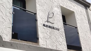 A building facade with a textured white exterior, two windows with dark blinds, and a central sign reading "ALOJAMENTO". - Piedra de Luna (Merida)