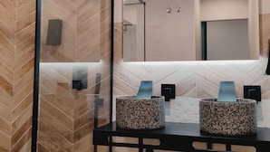 A modern bathroom with a herringbone wood pattern wall, a large mirror, and two granite sinks with blue accents. - Piedra de Luna (Merida)