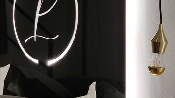 Un dormitori modern amb un signe de neó circular, un llit amb roba de llit blanca i gris, i un llum penjant.