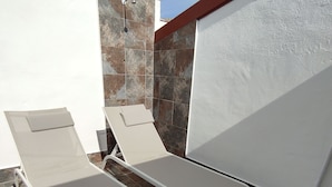 Two white sun loungers with metal frames on a tiled patio with a stone wall and white walls. - Piedra de Luna (Merida)