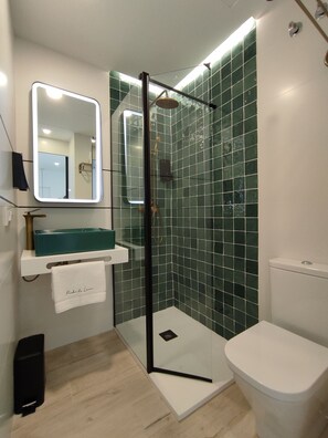 Un baño moderno con ducha de vidrio, un lavabo blanco y encimera verde azulada, y un inodoro blanco.