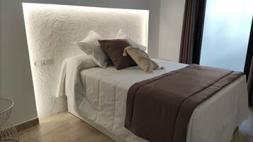 Een moderne slaapkamer met een gestructureerd hoofdeinde, een bed met wit en bruin beddengoed, en uitzicht op het omliggende landschap door een raam.