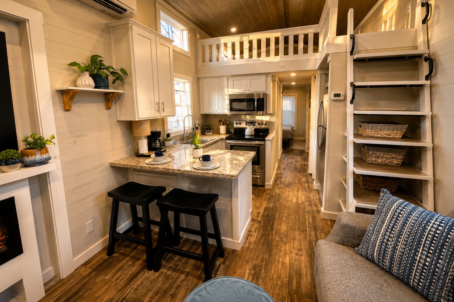 Cocina compacta con una isla central, taburetes de bar, microondas integrado y suelo de madera.