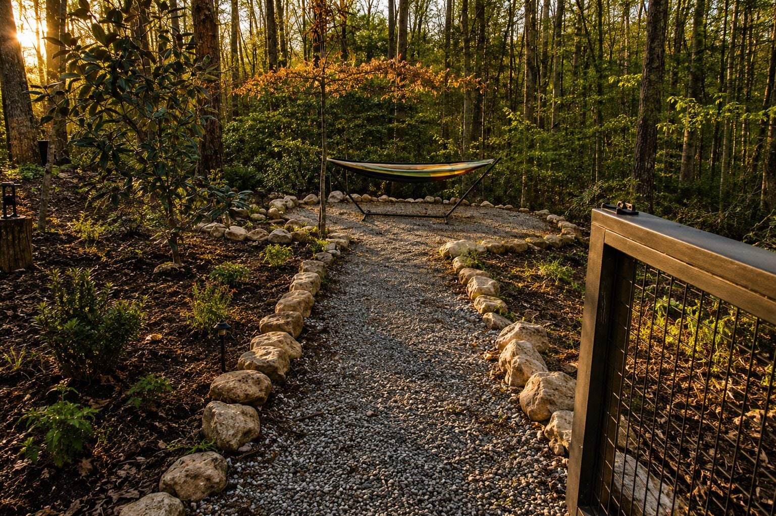 A gravel path bordered by rocks leading to a hammock in a forested area.