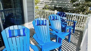 Drie blauwe Adirondack stoelen op een houten terras met een witte balustrade.