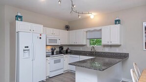 Een moderne keuken met witte kasten, een granieten aanrechtblad, een inbouwoven en een koelkast met waterdispenser.
