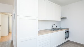 Una cocina moderna con muebles blancos, encimera de madera, pileta de acero inoxidable y horno integrado.