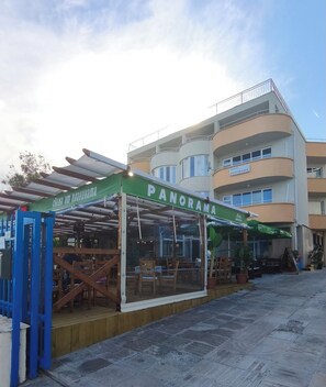 Ein Restaurant namens 'PANORAMA' mit Außenbestuhlung und Blick auf ein mehrstöckiges Gebäude im Hintergrund.