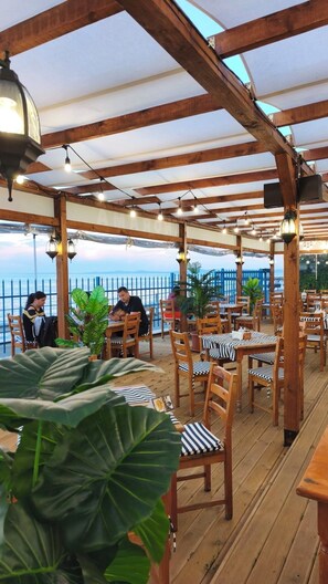 Ein Restaurant im Freien mit Holztischen und -stühlen, Lichterketten und Blumentöpfen.