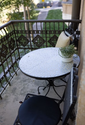 A round table with a mosaic top, a potted plant, and a chair on a balcony with a metal railing.