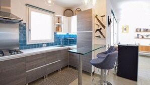 A modern kitchen with a gas stove, blue-tiled backsplash, and a glass bar stool. - Beautiful apartment in Sant'Antioco (Sant'Antioco)