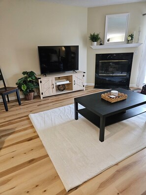 A living room with a TV, fireplace, wooden flooring, and a coffee table.