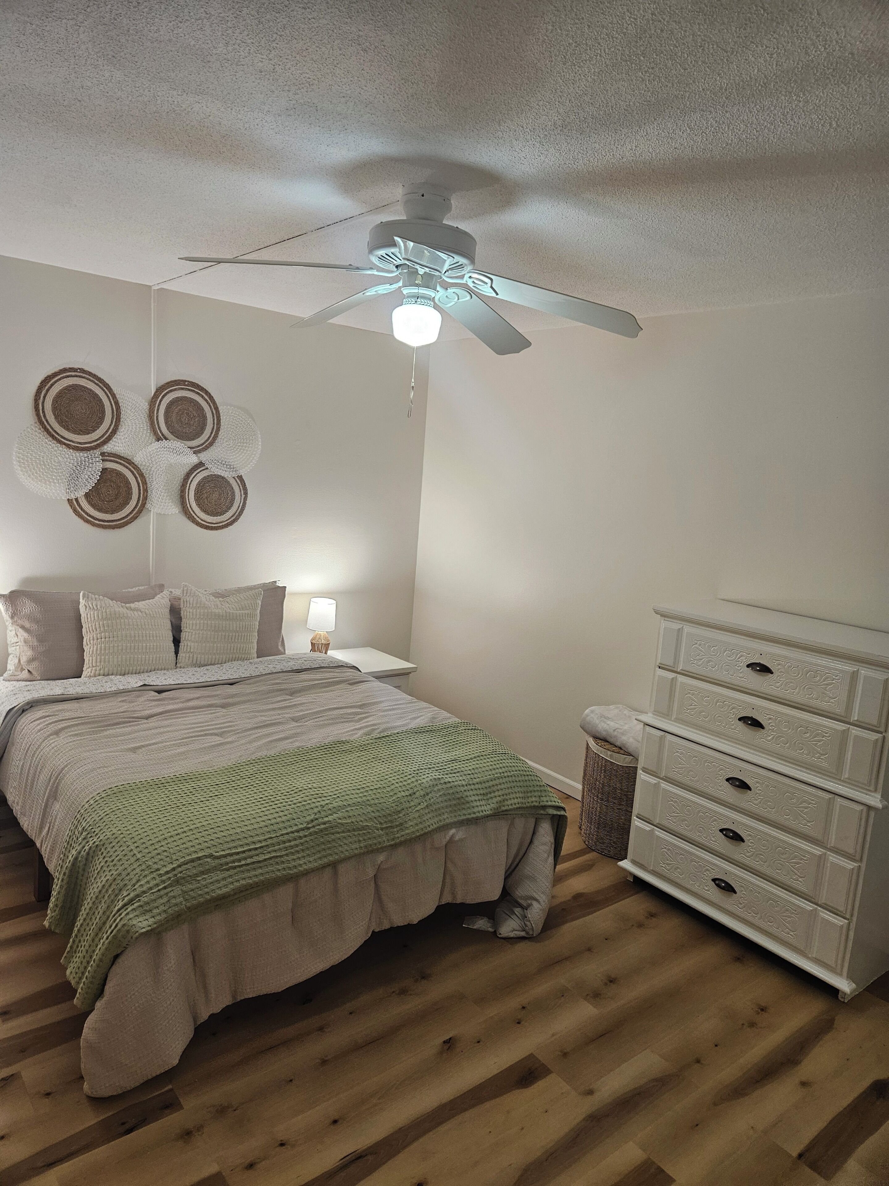 A bedroom with a bed, a dresser, a ceiling fan, and wall decor.