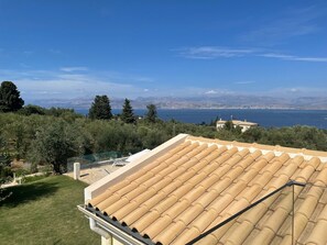 A rooftop terrace with a view of a coastal landscape, including trees and distant mountains.
