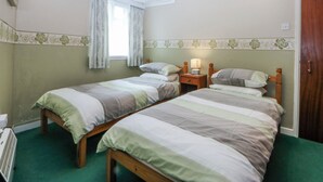 Una stanza con due letti singoli, un comodino con una lampada, una finestra con tende e un termosifone.