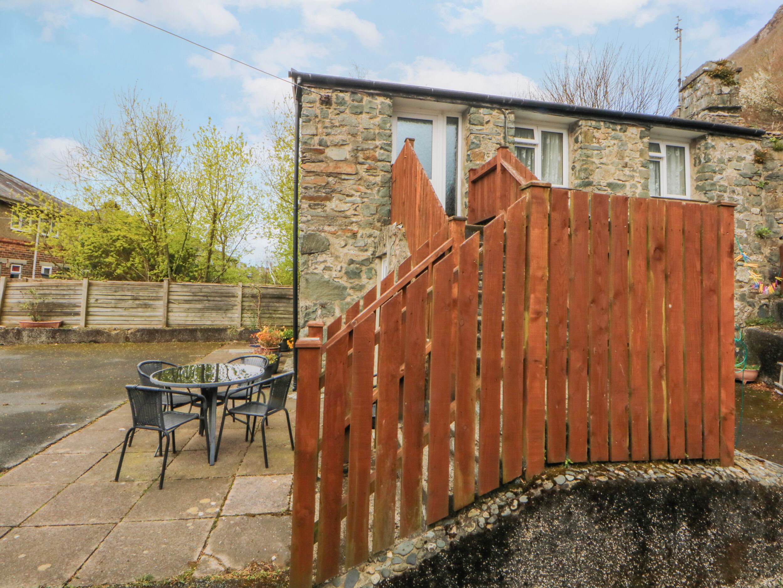 Une maison en pierre avec une clôture en bois, une terrasse avec des chaises et une petite table.