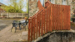 Una casa in pietra con un recinto di legno, un patio con sedie e un piccolo tavolo.