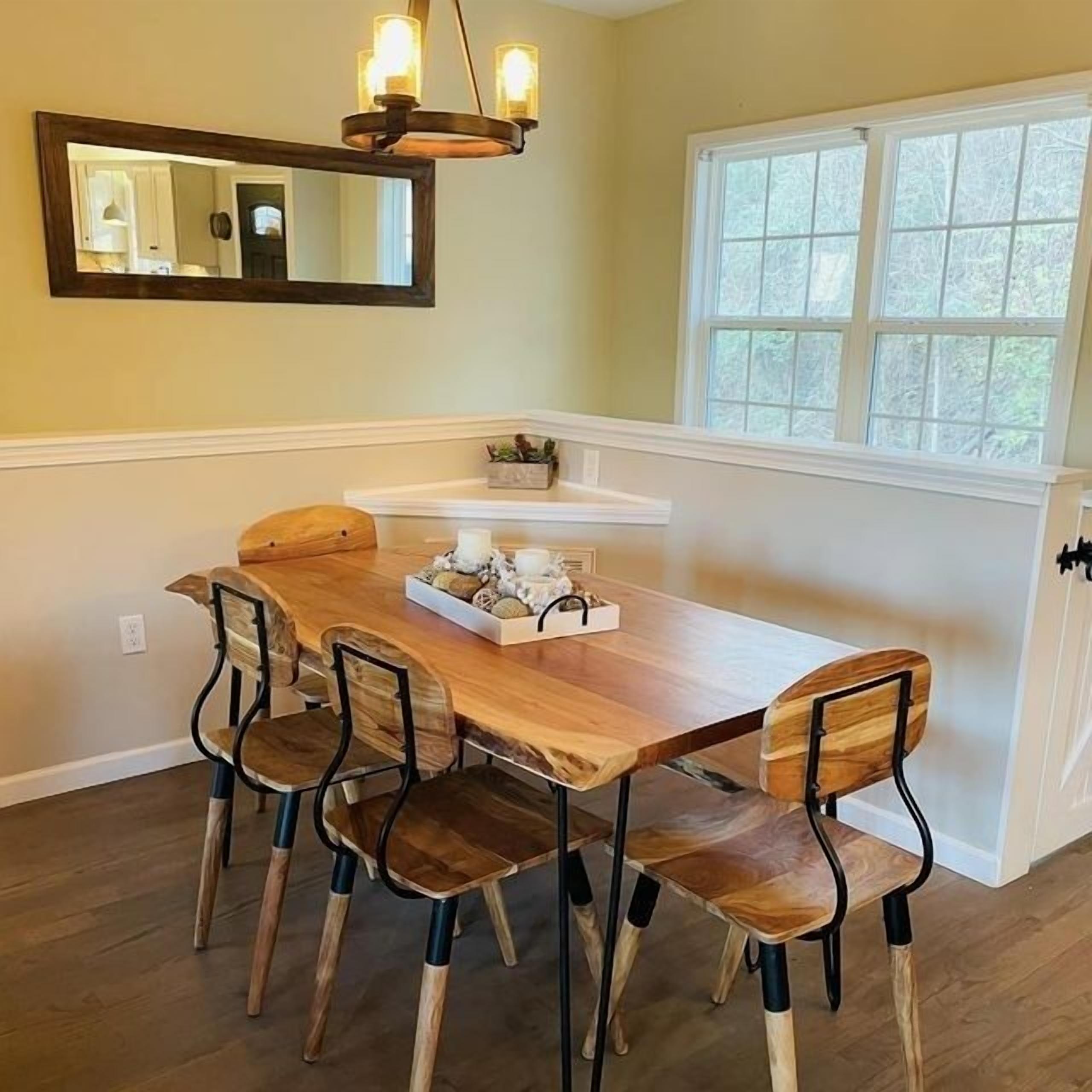 A dining area with a wooden table and chairs, a chandelier, and a window with a view of trees.