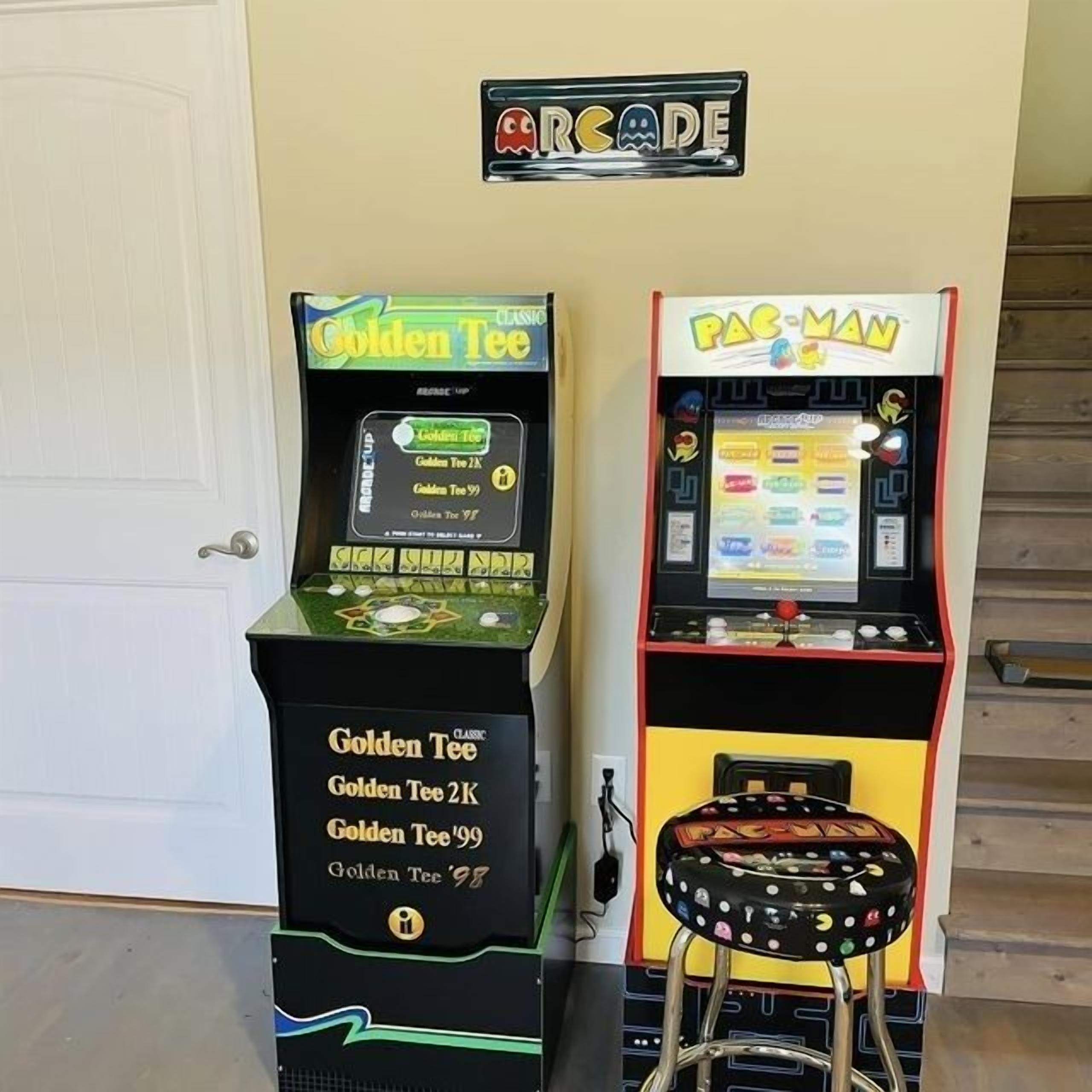 Two arcade machines, 'Golden Tee' and 'Pac-Man', with a stool in front of the 'Pac-Man' machine.