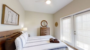 Une chambre à coucher comprenant un lit, une commode, un miroir, une horloge murale et une porte avec des stores.