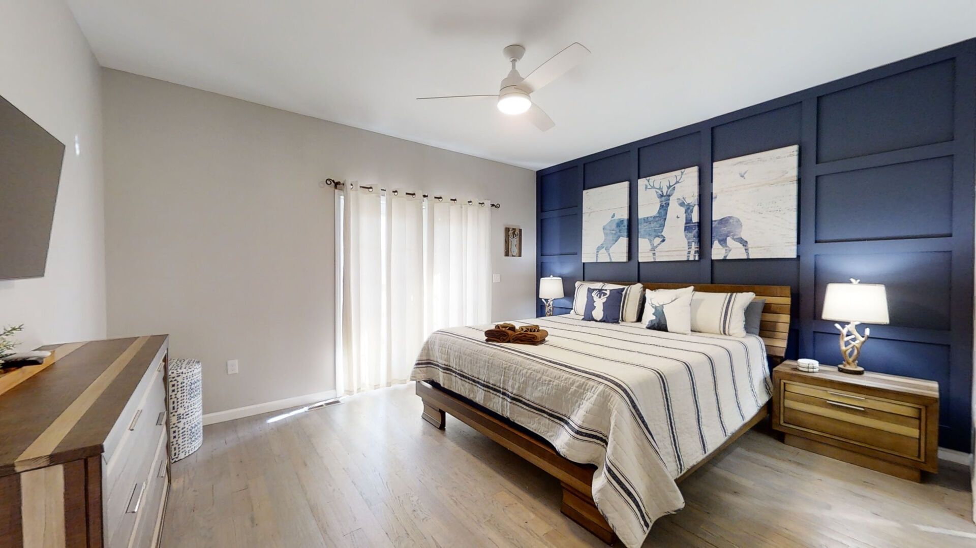 A bedroom with a bed, bedside tables, a ceiling fan, and artwork on the wall.