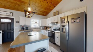 A modern kitchen with white cabinets, a stainless steel refrigerator, and a wooden ceiling.