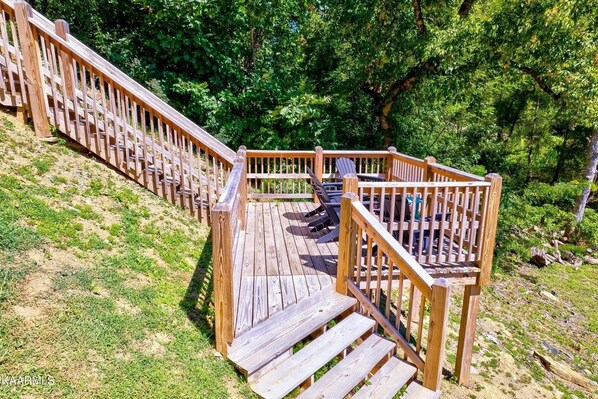 Une terrasse en bois avec des marches menant à un espace aménagé pour s’asseoir, entouré d’arbres.