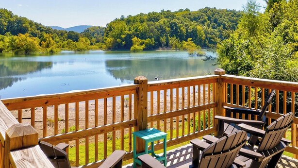 A wooden deck with outdoor seating and a view of a lake surrounded by trees.
