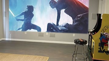A room with a large wall mural depicting a battle scene, a wooden floor, a small stool, and a gaming machine.