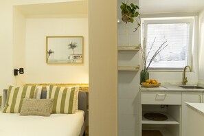 A compact hotel room with a bed, a small sitting area, a kitchenette, and a window with blinds. - Apartment by the river in Seixal bay. 3pax. Bicycles are available. (Seixal)