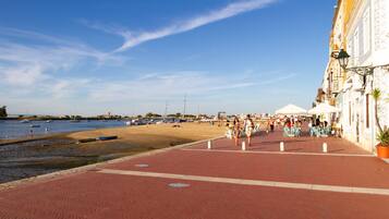 A waterfront promenade with a red brick walkway, boats, and a sandy beach.