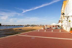 Une promenade en bord de mer avec un chemin pavé de briques rouges, des bateaux et une plage de sable.