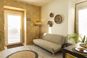 A modern living room with a sofa, a dining table with placemats, and a wall with decorative plates. - Apartment by the river in Seixal bay. 3pax. Bicycles are available. (Seixal)