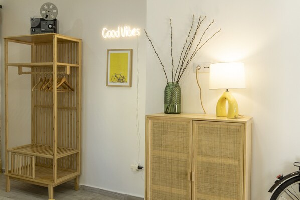 A room with a wooden wardrobe, a cabinet with a lamp, a neon sign, and a framed picture on the wall.