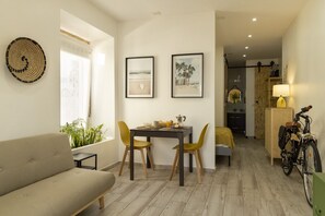 Un salon moderne avec un canapé, une table à manger et des chaises. On peut y voir un vélo et une lampe sur une table d’appoint.