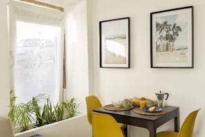 A dining area with a table set for breakfast, featuring a coffee pot, bread, and a fruit bowl.