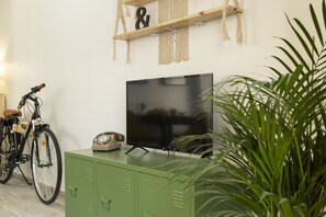 Une pièce avec un meuble vert, un vélo, une télévision et une plante.