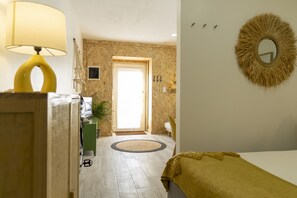 A hotel room with a bed, a lamp, a mirror, and a door leading to a hallway.
