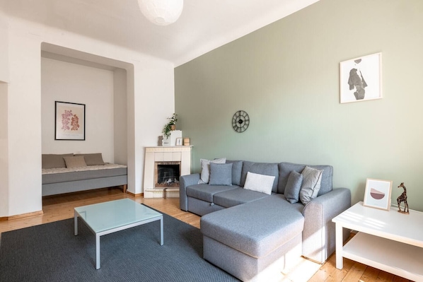 A modern living room with a grey sectional sofa, a glass coffee table, a fireplace, and a wall clock.