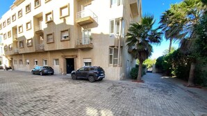 Un edificio residencial de varios pisos con un patio empedrado, autos estacionados y palmeras.
