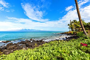 Ein tropischer Strand mit felsiger Küste, üppiger Vegetation und blauem Himmel.