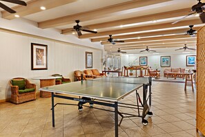 Ein geräumiges Zimmer mit Tischtennisplatte, Korbmöbeln, Deckenventilatoren und gerahmten Kunstwerken an den Wänden.