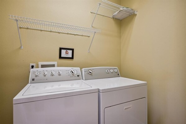 A laundry room with two stacked washers and dryers, a drying rack, and a framed picture on the wall.