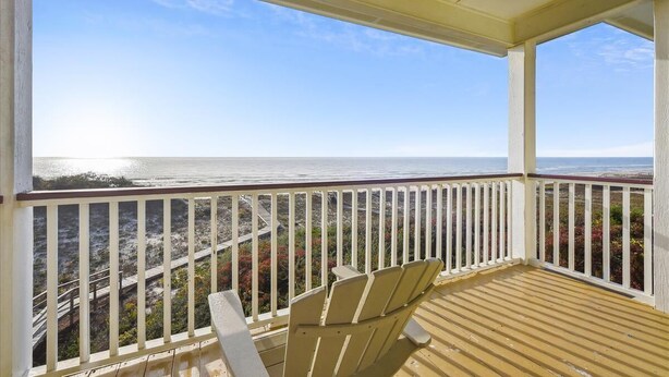 A covered balcony with a view of the ocean, wooden deck, and white railings.