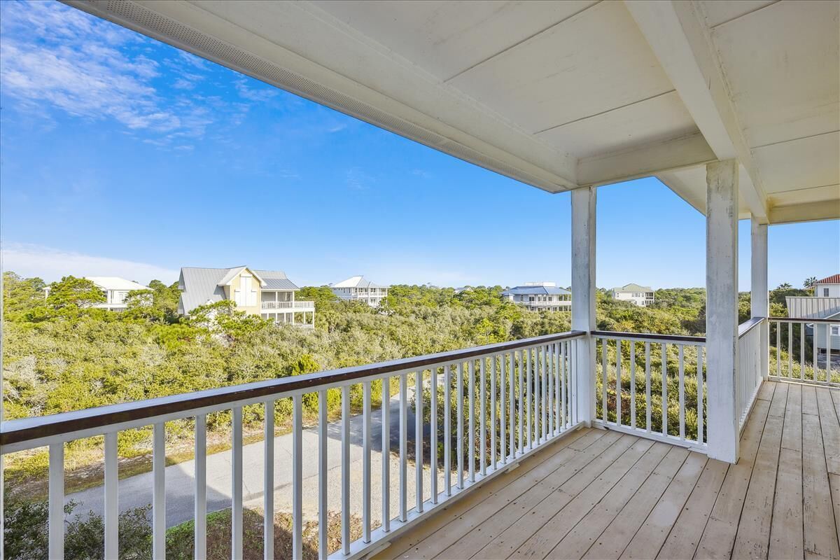 A wooden deck with a white railing overlooking a residential area with houses and greenery.
