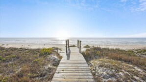 A wooden boardwalk leading to the beach with a clear sky above.